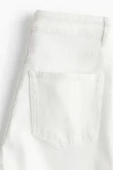Pantalón jean blanco de corte ancho, tiro alto y largo tobillero. Confeccionado en denim de algodón levemente elástico, con cinco bolsillos, cierre frontal con botón y pierna amplia.