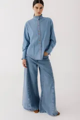 Camisa de jean celeste con cuello alto con volados y botones frontales.