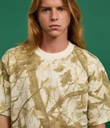 Remera de algodón color crudo con estampado de ramas y hojas en tonos marrones. Corte boxy, cuello redondo y mangas cortas.