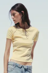 Camiseta corta de algodón color amarillo pastel, de corte recto, cuello redondo y manga corta. Detalle de costura marcada en la espalda.