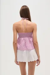 Top sin mangas confeccionado en algodón con estampado integral en tonos rosados. Presenta un diseño con cuello halter cruzado, pechera elástica con técnica de nido de abeja y bajo con volado tipo peplum.