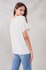 Remera blanca de corte holgado con estampado frontal de un recuadro violeta con la frase "Au jour d'hui!" en letras color naranja.