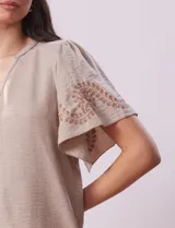 Blusa color beige de crepe, marca Batía, con cuello a la base y escote en V. Manga corta amplia con bordados.