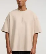 Remera oversized color beige confeccionada en gamuza sintética. Presenta cuello redondo, mangas cortas y bordado de cruz en el frente.