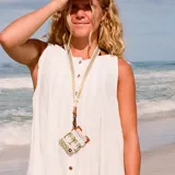 Llavero de cuello tipo lanyard con cinta de tela estampada con patrón de cuadros verdes y blancos. Presenta un detalle de parche en cuero sintético marrón con logo grabado, una estampa de palmera y un mosquetón metálico de color bronce.