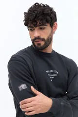 Buzo de algodón color negro lavado, con cuello redondo y estampado frontal en blanco con texto que incluye "BROOKSFIELD COVENT GARDEN LON UK". Presenta un pequeño parche negro en la manga izquierda.