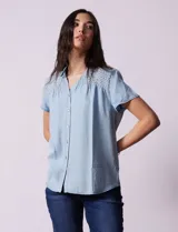 Camisa celeste de tencel con cuello con solapa, escote en V y abertura central con botones. Delantera con detalle en punto smock.