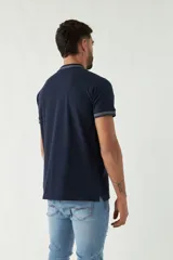Chomba azul marino de manga corta con cuello polo y detalles de líneas grises en cuello y mangas. Tiene logo bordado en el pecho. Corte regular.