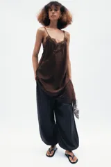 Vestido corto de satén color blanco, con tirantes finos, escote en pico y bajo asimétrico con abertura. Detalle de encaje negro en escote y ruedo.