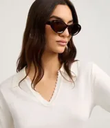 Blusa de punto color blanco, con cuello polo, escote en V y mangas cortas. Detalle de mini perlas aplicadas en el cuello.