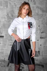 Camisa cropped blanca de mangas largas, con cierre frontal metálico y cuello clásico. Tiene un parche estampado con aplicaciones en el pecho.