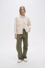 Sobrecamisa color crudo de corte recto, con cuello camisero, cierre frontal con botones metálicos a presión, mangas largas con puños abotonados, bolsillos de parche en el pecho y ruedo recto.
