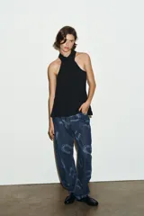 Top negro con cuello halter ajustable con lazada y hombros descubiertos. Presenta cierre lateral con cremallera oculta.