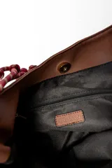 Bolso marrón con forma de media luna y asa de soga trenzada en rojo y blanco.