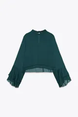 Camisa verde esmeralda de cuello alto y manga larga con volantes en los puños. Cierre en la espalda con abertura y botones.