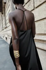 Vestido midi negro de satén con escote en pico, tirantes finos y aplique dorado con cadena en el hombro.