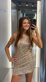 Vestido corto ajustado color dorado con lentejuelas, de corte asimétrico con un solo hombro descubierto.