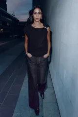 Jersey de punto negro, sin mangas (manga sisa), con cuello cuadrado drapeado y un broche dorado decorativo en el hombro.