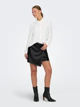 Minifalda negra de cuero sintético con corte cruzado y tachas plateadas en forma de estrella.