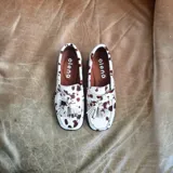 Mocasines de cuero con estampado animal print de vaca, con borlas decorativas y suela plana.