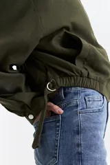 Campera corta color verde militar, sin cuello, con cierre frontal y elástico en la cintura. Tiene bolsillos amplios y mangas largas con puños elásticos.