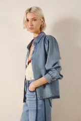 Camisa celeste de tencel, de calce recto, con manga larga amplia con frunces en los hombros y cuello camisero. Mangas terminadas en puño con botón y ojal. Cartera delantera con botones metálicos con el logo de la marca.