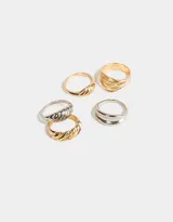 Set de cinco anillos de metal con diferentes diseños: uno dorado con textura de líneas horizontales, uno plateado con textura trenzada, uno dorado con forma de croissant, uno dorado con textura de líneas horizontales y uno plateado con diseño doble.