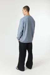 Buzo de manga larga color celeste grisáceo con cuello redondo y un pequeño logo bordado en forma de 'X' azul marino en el pecho.
