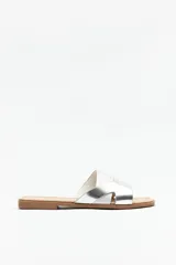 Sandalias bajas plateadas con tiras anchas cruzadas en el empeine y suela plana color marrón.