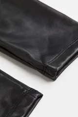 Calza de cuero sintético color negro, de tiro alto y corte ajustado.