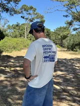 Remera beige de manga corta con estampado gráfico en azul en la espalda que incluye el texto "BROKERS GRAPHIC RESEARCHING" y "THE NEW WAVE BROKERS".