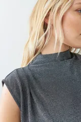 Blusa plateada de lurex con cuello alto y tablas en los hombros. Sin mangas.