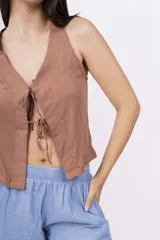 Chaleco corto sin mangas color verde salvia, confeccionado en tela perforada (broderie o calado). Presenta escote en V con lazos ajustables en el centro frontal.