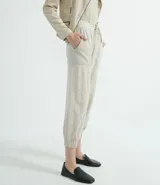 Pantalón jogger color beige, con elástico en la cintura y en los tobillos, cordón ajustable, bolsillos laterales y detalles de agujeros en los laterales y en los bolsillos.
