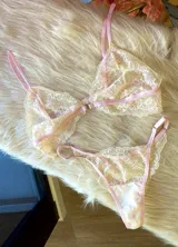 Conjunto de lencería de encaje floral en tonos rosa y crema, compuesto por un corpiño triangular sin aro con breteles finos regulables y una tanga regulable.