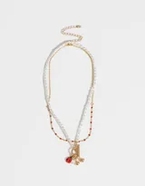 Set de dos collares dorados: uno de cadena con mostacillas rojas y otro de perlas con cierre marinero y dijes de vaquita de San Antonio, cerezas y perla.