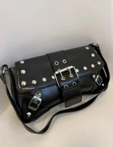 Cartera negra con correa corta para el hombro, con apliques de tachas y hebillas plateadas.