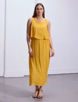 Vestido largo color mostaza de crepe, marca Marissa Olivia. Escote redondo con sobrecapa y detalle de crochet en los hombros. Corte en la cintura con punto smock. Sin mangas.
