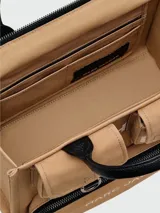 Bolso tote mediano de lona color beige con detalles en negro. Tiene doble asa de mano de cuero y correa bandolera ajustable y extraíble. Cuenta con dos bolsillos frontales con solapa y un bolsillo frontal con cierre. Estampado frontal con la leyenda "THE TOTE BAG" y el logo "MARC JACOBS".