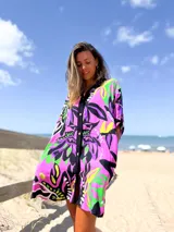 Camisero de manga corta, corte holgado, con cuello camisero y botones frontales. Presenta un estampado vibrante de motivos florales en tonos fucsia, negro, lila, verde lima y amarillo.