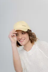 Gorra de béisbol color amarillo pastel, con visera curva y logo de Peach bordado en el frente. Ajustable en la parte trasera.
