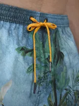 Short de baño verde con estampado de margaritas blancas y cordón ajustable naranja.
