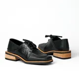 Zapato acordonado de cuero vacuno color marrón oscuro, con suela de goma, horma cuadrada y tacón bajo.