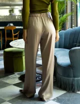 Pantalón palazzo de tiro alto color violeta, de satén. Tiene pretina delantera con pasadores, botón y cierre, pretina trasera elastizada y bolsillos verticales delanteros.