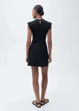 Vestido corto negro con cuello Perkins y corte peplum. Sin mangas y con cierre de botón en la parte posterior.
