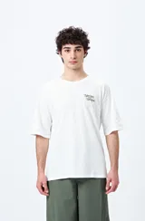 Remera blanca de corte holgado con mangas cortas y cuello redondo. Estampado pequeño en el frente con la frase "Spritz and Shine" en verde.
