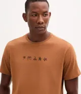 Remera masculina de algodón color tostado, con cuello redondo y manga corta. Presenta un estampado localizado de íconos playeros en negro en el pecho.