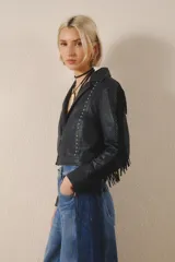Campera corta de cuero color negro, con flecos en espalda y mangas, tachas metálicas y símil piedra cristal. Cierra con broches en el frente, tiene forrería y bolsillo interno.