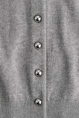 Cárdigan gris de punto suave con cuello redondo y botones metálicos dorados en el frente. Tiene remate acanalado en cuello, puños y bajo.