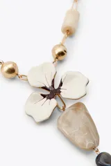 Collar con cadena dorada de eslabones y cuentas de resina en tonos beige y blanco. Dije central con forma de flor esmaltada y colgante con piedras de diferentes tamaños y colores.
